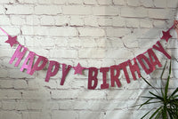 Happy Birthday banner with pink and red letters against a white brick wall.