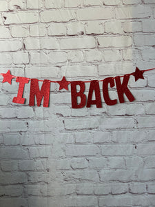 Red 'I'm Back' sign with stars on a textured white wall